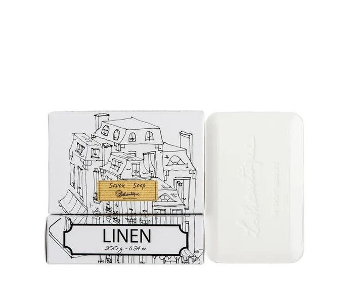 A white box of Lothantique bar soap with a drawing of a cityscape and labelled with the scent Linen, beside a white bar of soap.