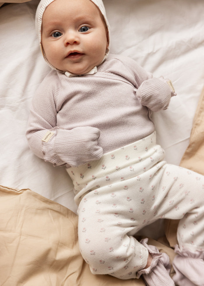 Baby in light purple bodystocking with long sleeves and front snap closure.