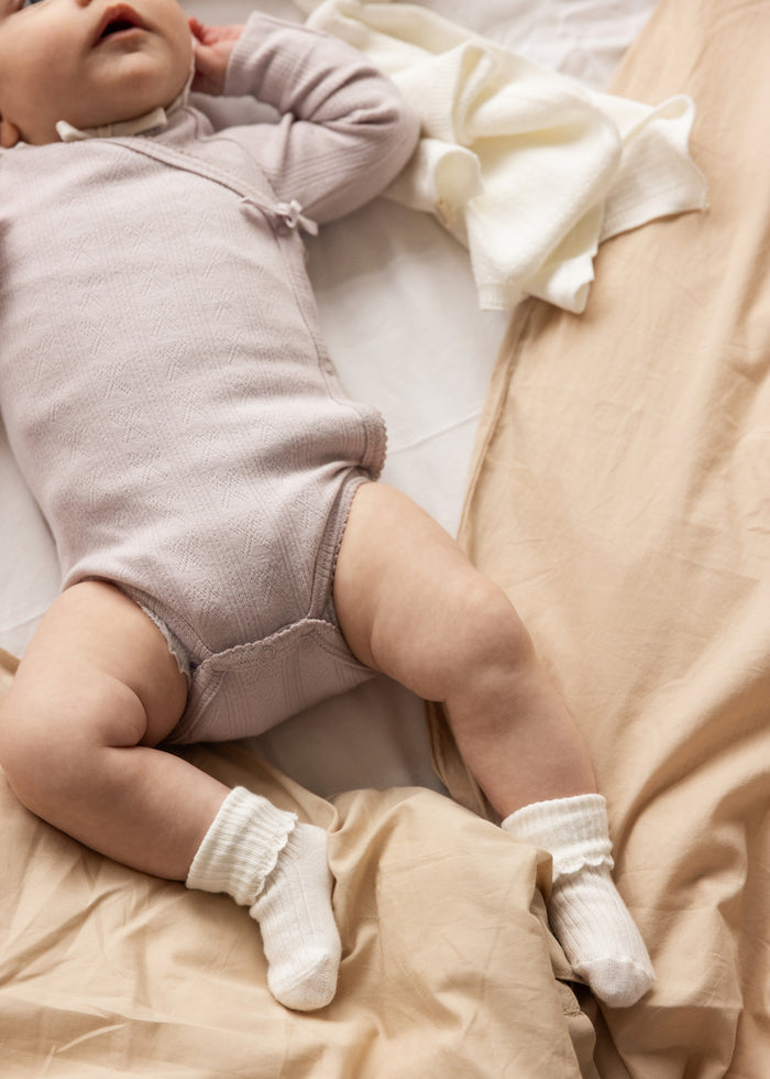 Baby bodystocking in light purple with long sleeves, visible seams at the legs.