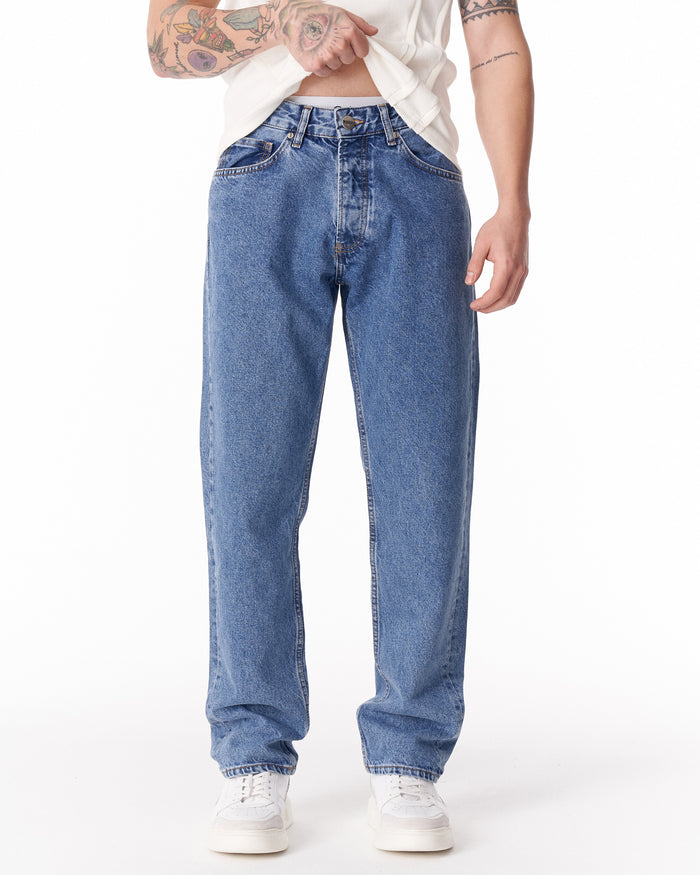 Martin Valen blue loose-fit men's jeans, front waist view with visible button and model lifting shirt