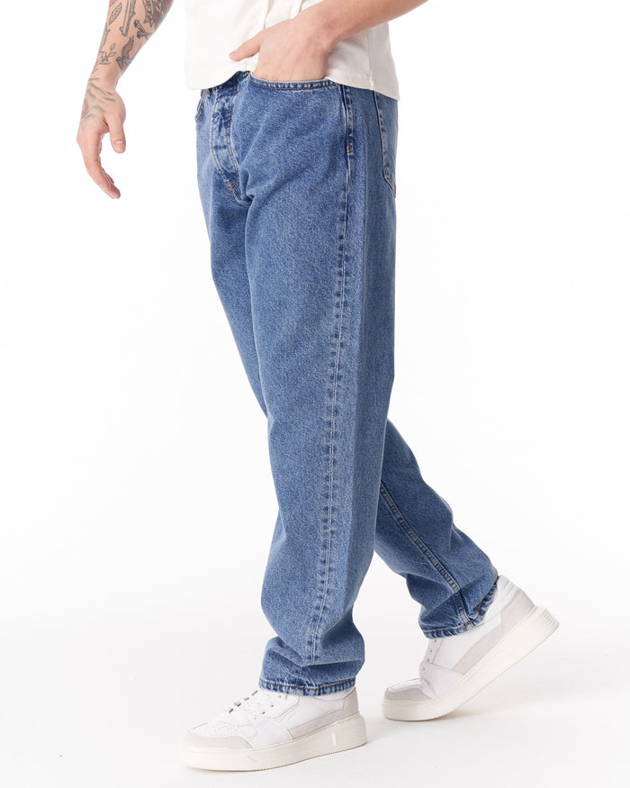 Martin Valen blue loose-fit jeans, three-quarter leg view showing stacked hem and white sneakers