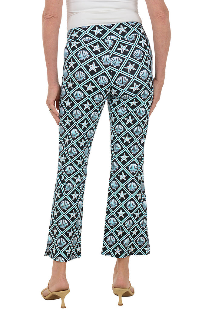Woman wearing patterned seashell pants with a white top on a white background. Back shot.