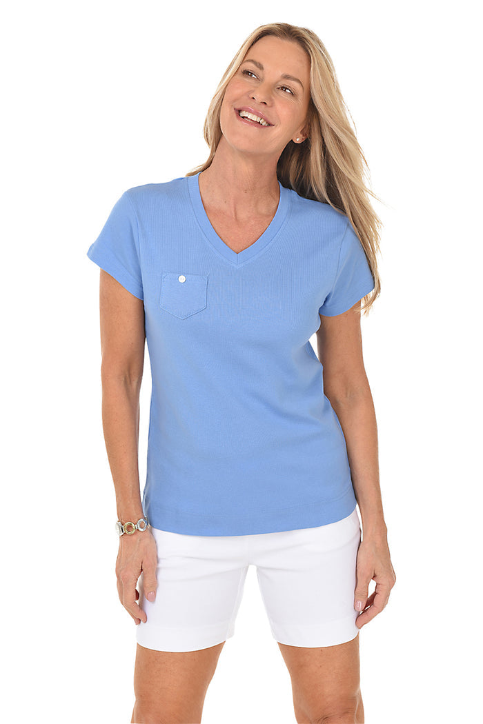 Woman wearing a light blue scrub top with a pocket and white shorts on a white background