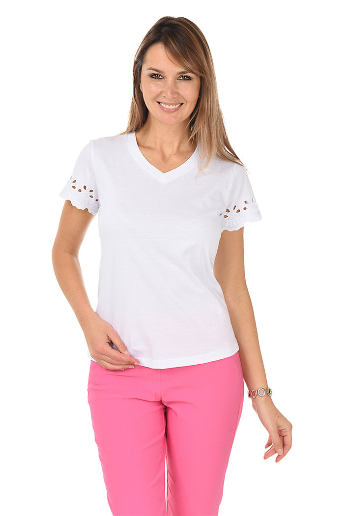 Woman wearing a white top with lace details and pink pants on a white background.