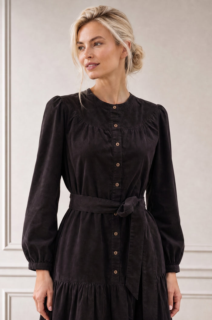 Model wearing the Aspiga Baby Cord Midi Dress in Chocolate, a chocolate brown corduroy belted shirt dress with long sleeves and a collar, alternate view