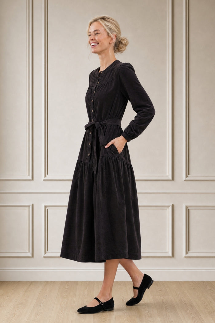 Model wearing the Aspiga Baby Cord Midi Dress in Chocolate, a chocolate brown corduroy belted shirt dress with long sleeves and a collar, alternate view