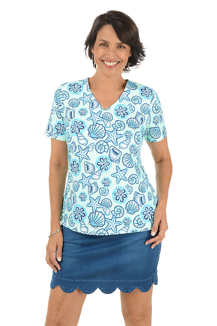Woman wearing a blue patterned blouse with a shell design and a scallop denim skort on a white background.