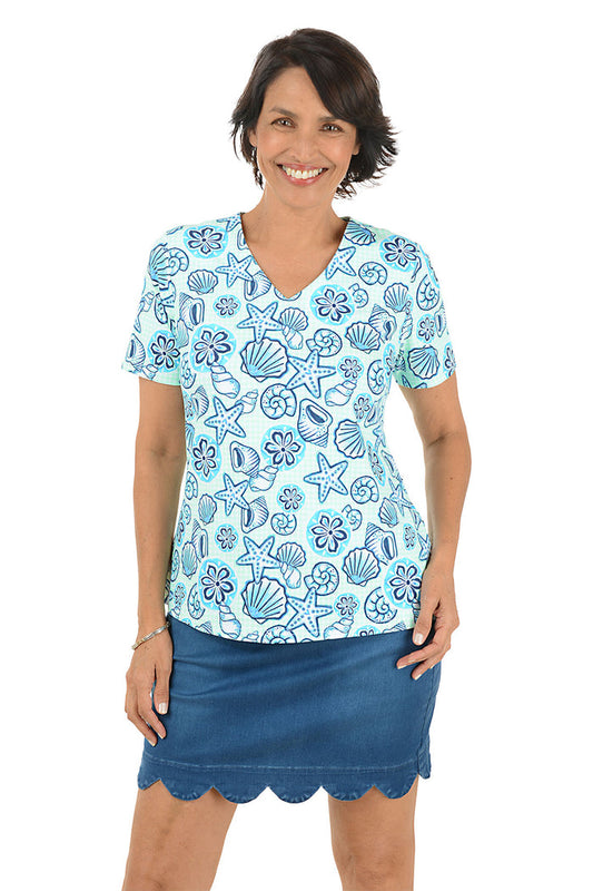 Woman wearing a blue patterned blouse with a shell design and a scallop denim skort on a white background.