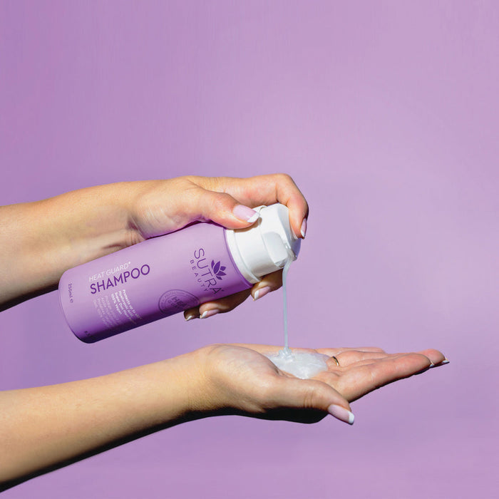 A person dispensing creamy shampoo from a lavender bottle labeled Heat Guard Shampoo | SUTRA onto their palm against a soft purple background.
