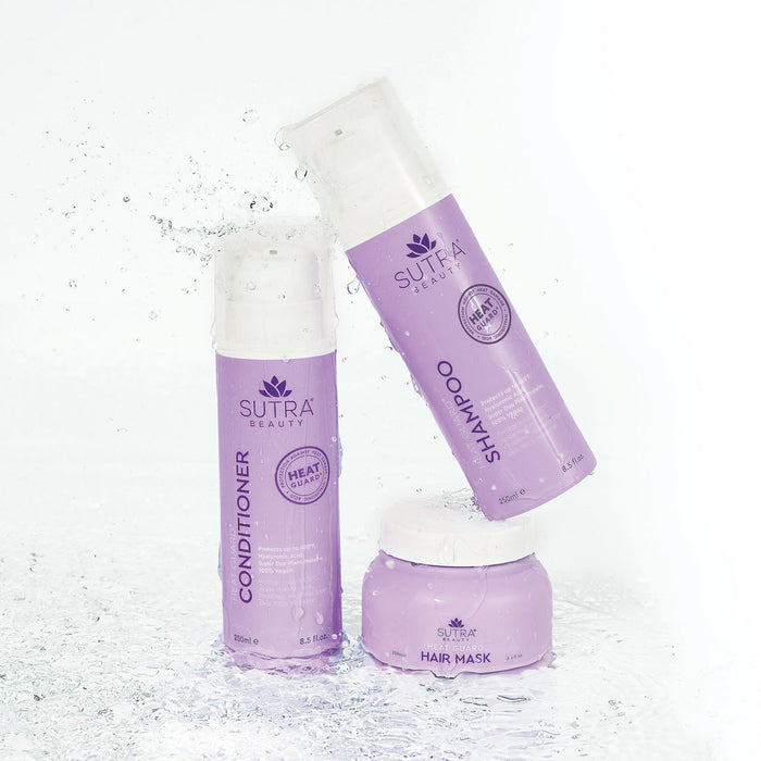 Three lavender-colored SUTRA Beauty hair care products with water splashes, featuring Heat Guard Shampoo | SUTRA in the center.