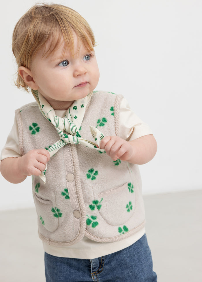 Baby wearing a beige vest with green clover print and buttons.