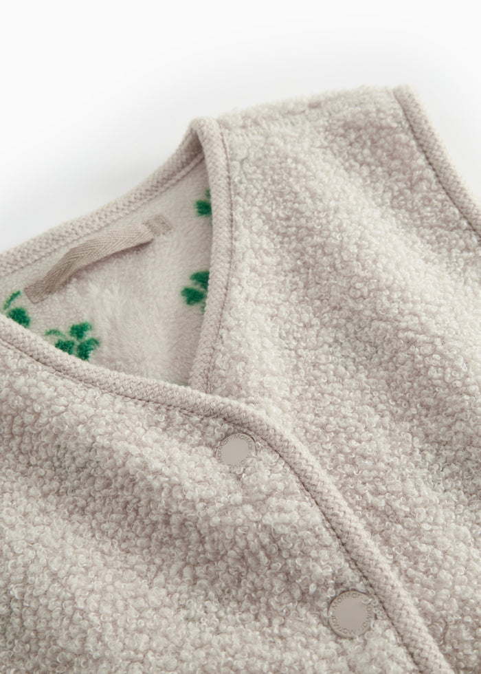 Details of a beige teddy vest for children with a green clover print, snap buttons, and soft structure.