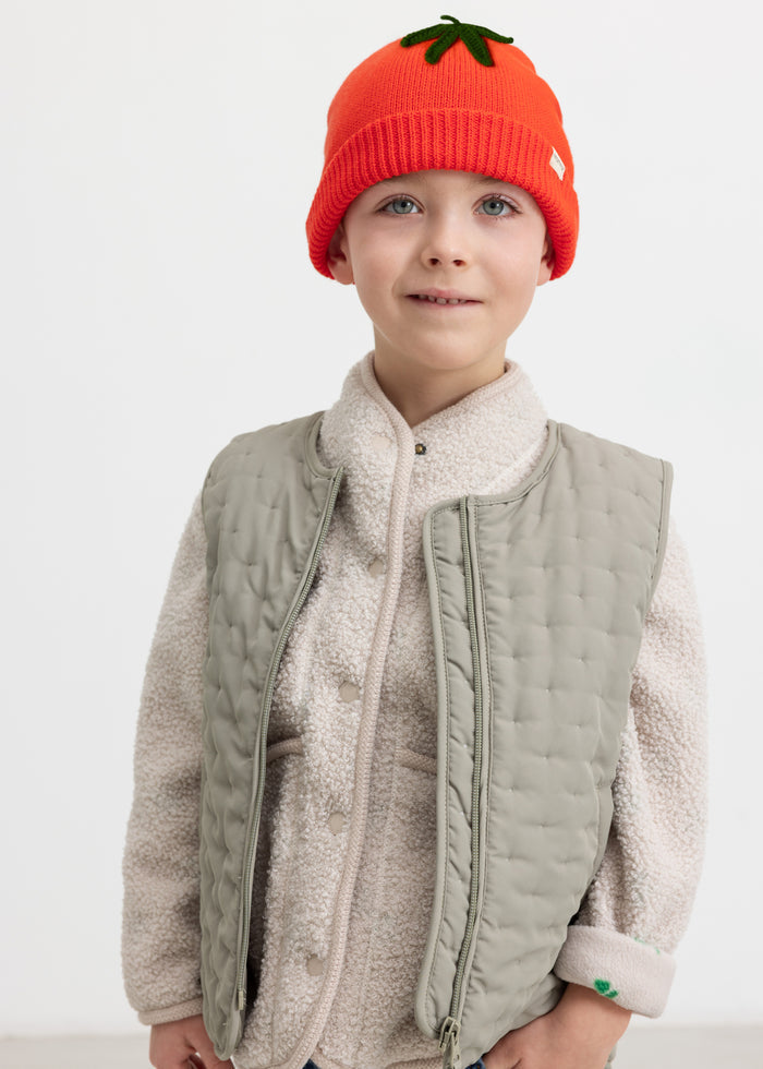 Child wearing a beige fleece jacket and a red knitted hat.
