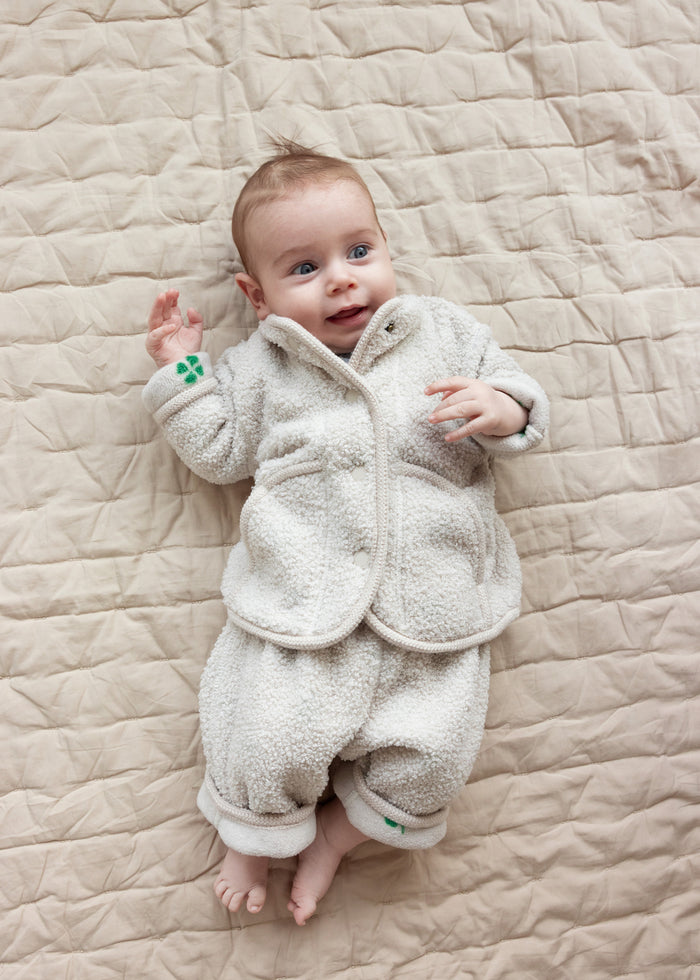 Baby wearing a beige fleece jacket and matching pants lying on a blanket.