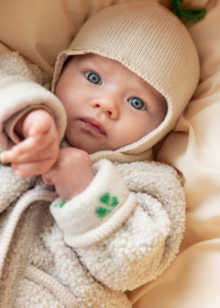 Baby in beige fleece jacket and beige knitted hat set close to