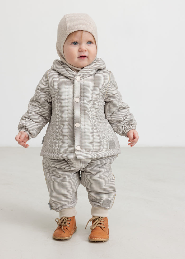 Baby wearing a plaid thermal jacket and matching pants, as well as a beige knitted hat.