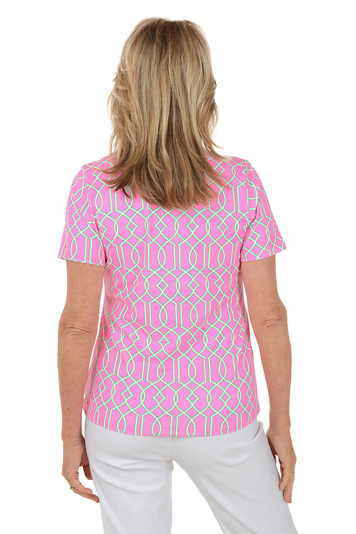 Woman wearing a pink patterned blouse with white pants on a white background. Back shot.