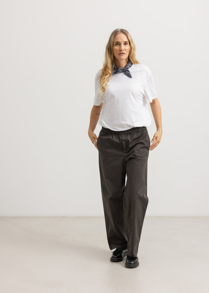 Dark pants on model with elastic waistband and straight, loose falling legs.