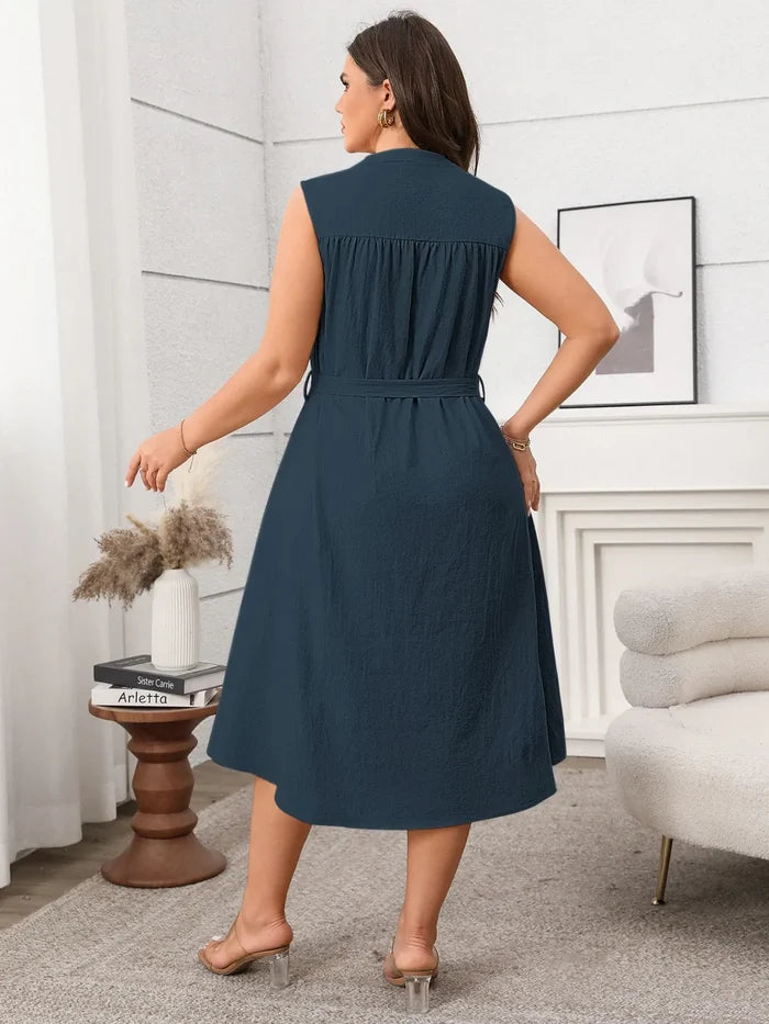 Woman wearing sleeveless tie waist plus size dress in navy blue standing in modern living room