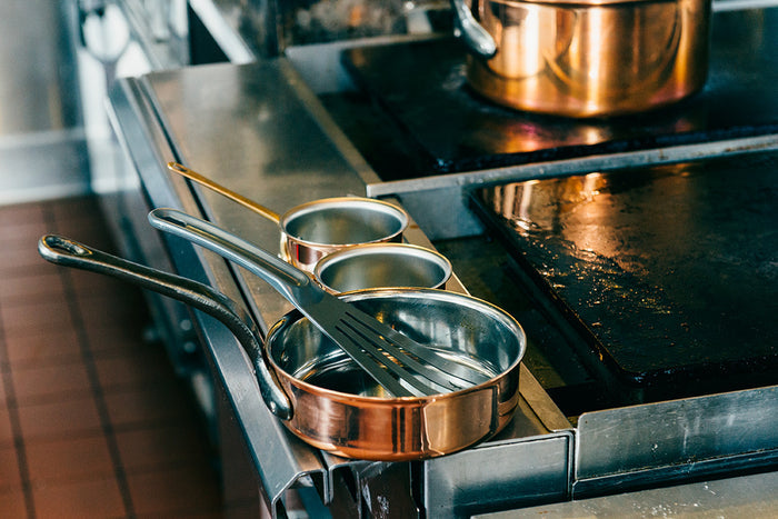 Set of copper cookware on a stovetop with grey slotted spatula in cookware.