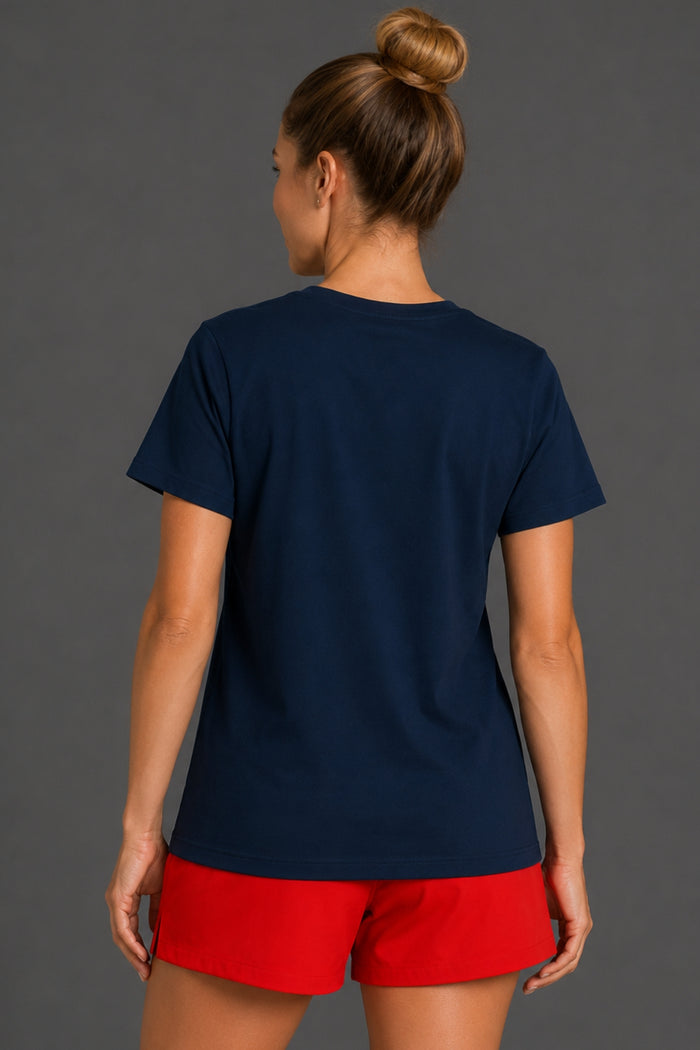 A woman shown from the back wearing a navy blue short-sleeve t-shirt and bright red shorts against a dark gray studio background. || Navy