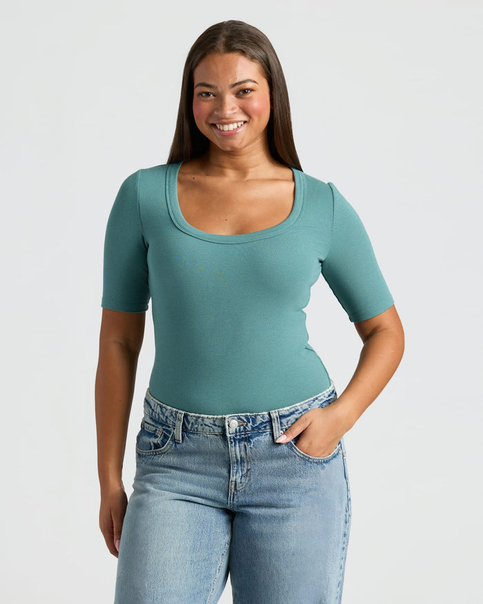 Woman wearing a teal top and blue jeans on a plain background
